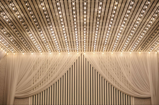 close up photo of a white ceiling and a part of a wall decorated with drape and lights